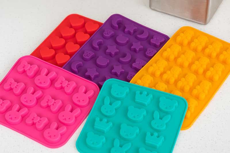 A collection of colorful and fun-shaped silicone candy molds on a clean kitchen counter.
