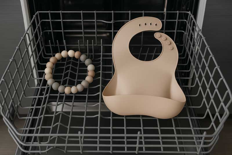 Silicone beads and a silicone bib sitting securely on the top rack of a modern dishwasher.