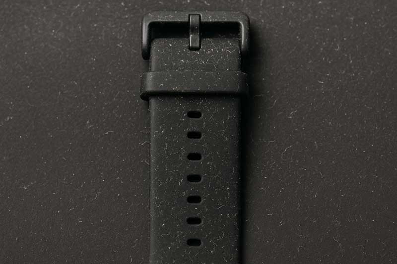 A black silicone watch strap showing visible dust and lint particles clinging to its surface.