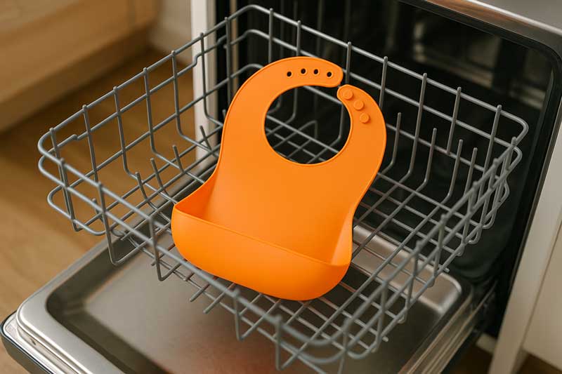 A brightly colored silicone bib sitting securely on the top rack of an open dishwasher.