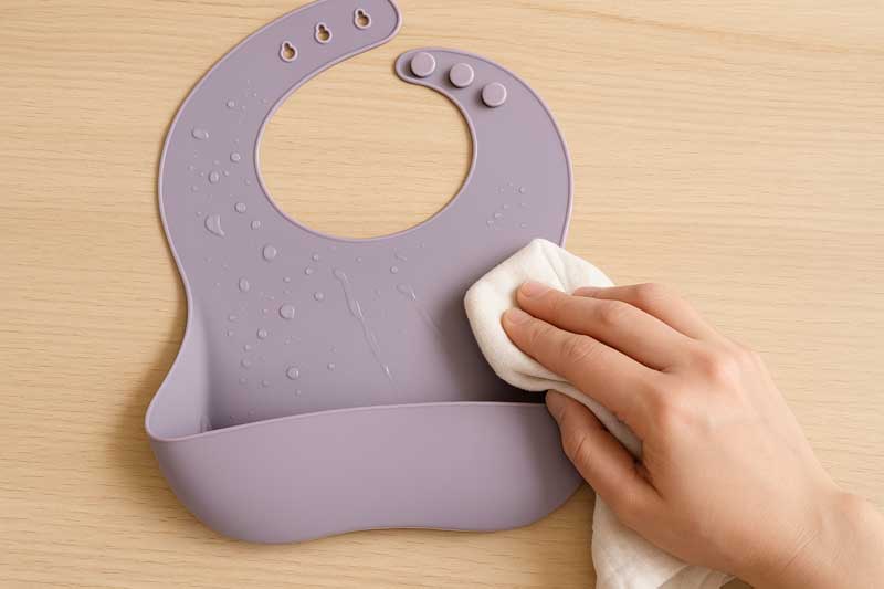 A hand quickly and easily wiping a wet silicone bib with a dry cloth.